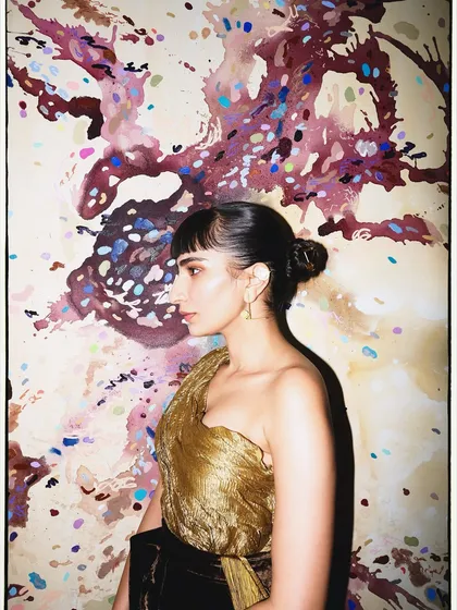 A profile shot against an artistic backdrop, highlighting the texture of the antique gold sculpted top.