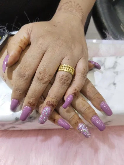 A full set of long, square-shaped extensions in a solid mauve-purple color. To add some glamour, the ring finger on each hand is coated in a dense, sparkling silver glitter. This is a great way to elevate a simple color.