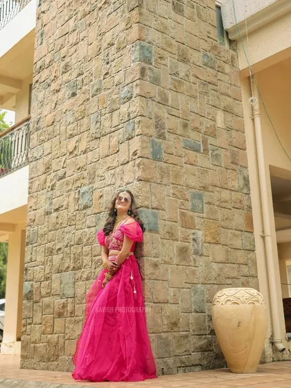 A full-length shot of the bride in a vibrant pink outfit, posing against a stone wall.