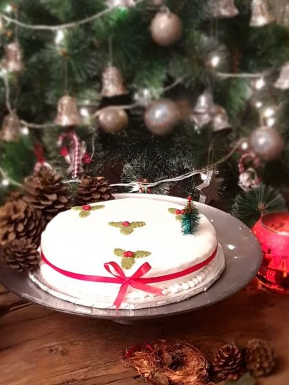 A beautifully decorated Christmas cake with white icing and holly details, set against a festive backdrop. A perfect centerpiece for your Christmas dinner.
