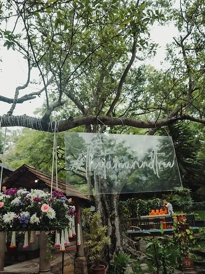 A clear sign hanging from a tree, a modern and elegant way to welcome guests to the wedding.