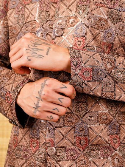Royalty woven in every thread. A close-up on the sleeve of a brown patterned jacket, showing the intricate geometric embroidery.