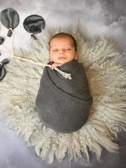 Floating away on a cloud of dreams. This creative shot features a swaddled newborn holding a bouquet of grey balloons, creating a whimsical and artistic portrait.