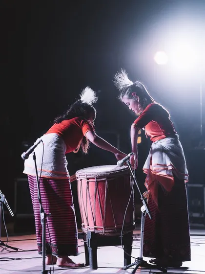 Two performers prepare their large drum on stage, backlit by a powerful spotlight. This behind-the-scenes style shot captures the anticipation before the music starts.