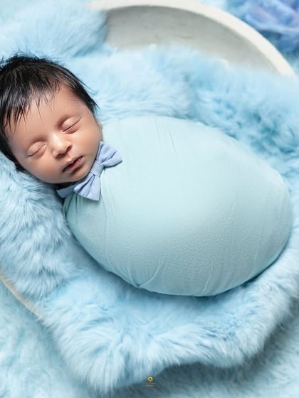 A classic potato sack pose, where the baby is snugly wrapped and placed in a bowl lined with soft blue fur. The tiny bow tie is the perfect finishing touch.