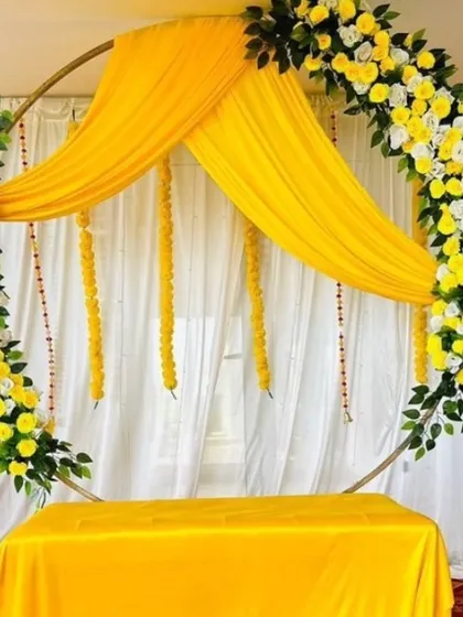 A simple and elegant backdrop for a Haldi or Mehandi ceremony. The circular frame is decorated with yellow and white flowers and draped with yellow fabric.