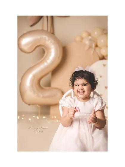 A big, happy smile for her second birthday! The soft, neutral colors and twinkling lights create a warm and celebratory feel.