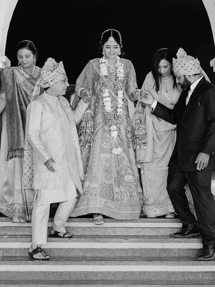 A black and white photo of a bride being carefully escorted down the stairs by her family. This image captures the support and love surrounding her as she makes her way to the ceremony.