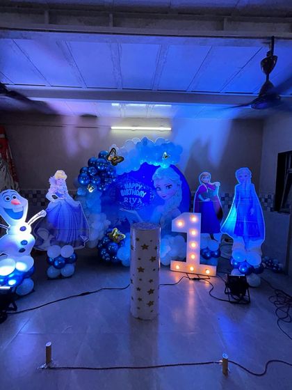 An enchanting 'Frozen' theme for a first birthday, with illuminated character cutouts of Elsa, Anna, and Olaf creating a magical, glowing effect in the dark.