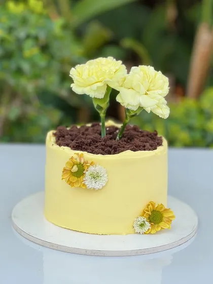 Our mini "Bloom" cakes are designed to look like little pots of love. This one features a moist lemon and cream cheese cake with a yellow frosting, topped with chocolate crumble "soil" and fresh carnations. It’s a whimsical and creative dessert perfect for gifting.