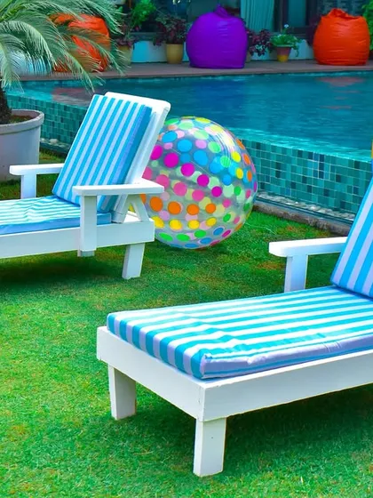 Classic poolside loungers with striped cushions, set up on the grass with colorful beach balls to complete the summer vacation vibe.