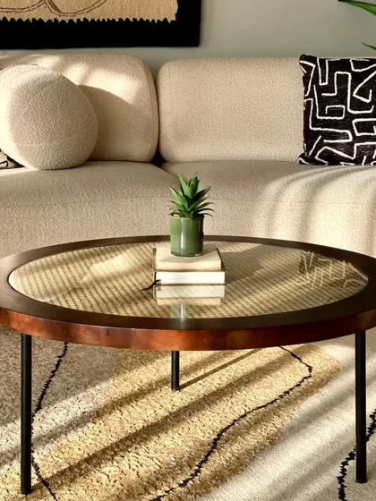 I love combining traditional materials with modern designs. This centre table features a classic rattan weave protected by a glass top, set in a dark wood frame with sleek metal legs, perfect for a contemporary living room.