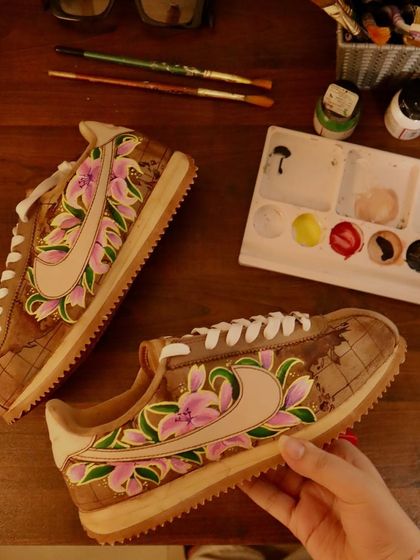 This design combines a love for travel and nature. I started with a coffee-dyed base on these Nike Cortez, painted a vintage world map, and then layered beautiful lilies over it, which were my client's favorite flower.