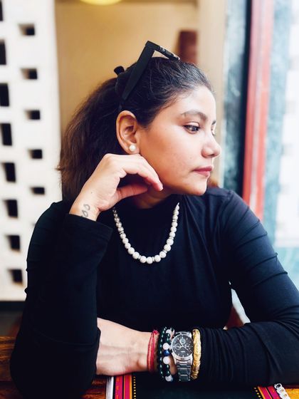 A pensive moment at a cafe. This close-up shows how classic accessories like a pearl necklace and a simple watch can elevate a simple black turtleneck.