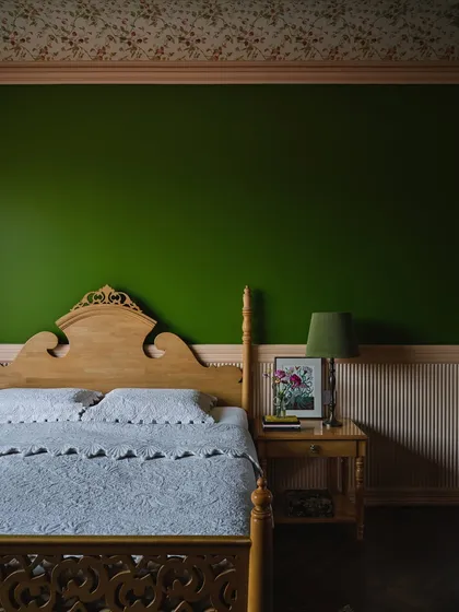 A detail of the artist's bedroom, showing the bold contrast between the forest green wall and the warm wood of the refurbished bed. Framed artworks and fresh flowers complete the picture.