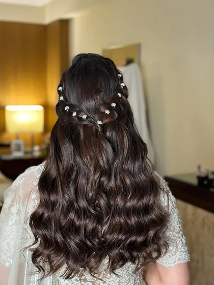 A half-updo with a crown braid, adorned with small pearl flowers, perfect for a welcome dinner or engagement.