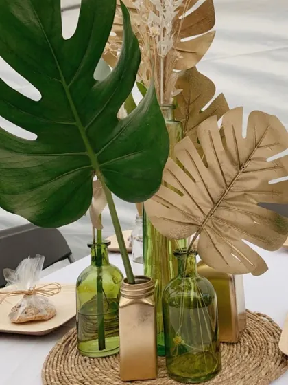 A touch of gold can elevate any decor. For this tropical-themed setup, I spray-painted monstera leaves gold and placed them in green glass vases for a chic and modern centerpiece.