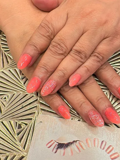 A lovely coral-colored set of almond nails. Two accent nails on each hand are covered in a fine, matching coral glitter for a cohesive and sparkly look.