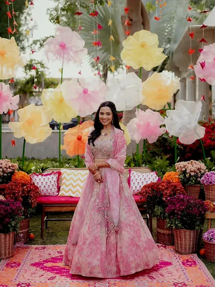 A full-length shot of the bride standing in front of the beautiful paper flower wall, smiling for the camera.