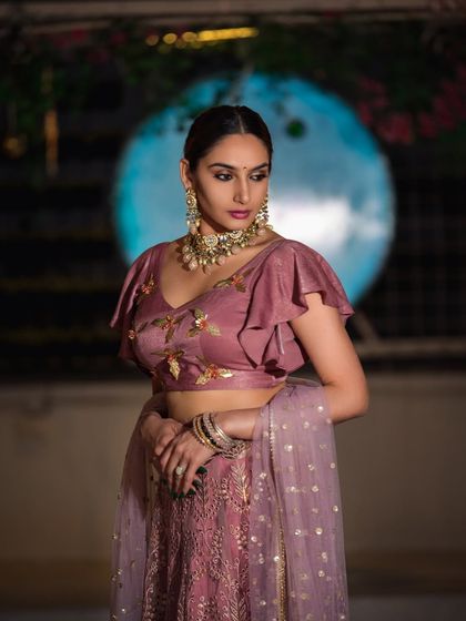 An elegant evening look for an ethnic wear collection, shot outdoors. The soft background lighting helps the model and the detailed embroidery on her blouse stand out.