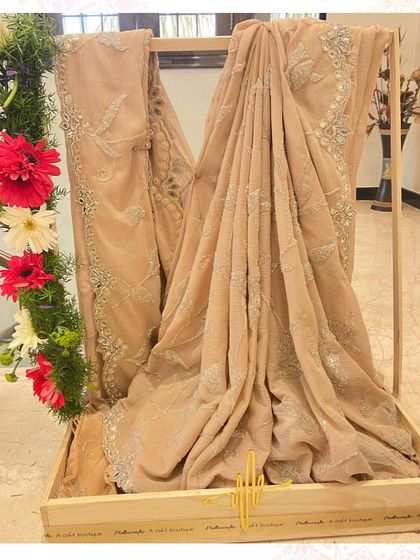 A neutral-toned embroidered saree presented with a simple floral arrangement, letting the craftsmanship of the garment speak for itself in this trousseau display.