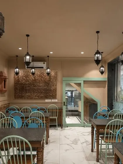 The dine-in space at Shiv Mishthan Bhandar features walls clad with lakhori bricks and traditional mouldings. Large glass panels create an interactive experience, connecting diners with the vibrant street life of Old Delhi.