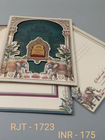 A multi-layered invitation with a die-cut archway revealing a deep teal background. The design is framed with royal elephants and floral patterns, and includes three inserts for event details.