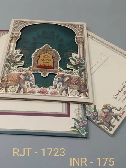 A multi-layered invitation with a die-cut archway revealing a deep teal background. The design is framed with royal elephants and floral patterns, and includes three inserts for event details.
