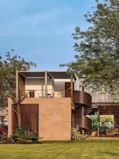An alternate view of the Abhikram residence, showing the interplay between the solid brick structure, the open patio, and the sculptural form of the external staircase.