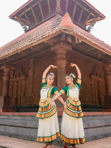 A wide shot of two dancers in front of a traditional temple structure. This image captures the grandeur of the dance form and its cultural context.