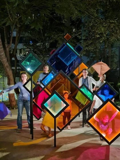 People interacting with the transformed 'Family Tree' installation, now adorned with colorful panels. The piece evolves with the seasons and festivals, reflecting the multicultural spirit of Mumbai.