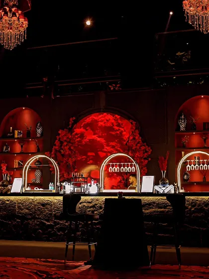 The heart of the party. This magnificent bar setup features a backdrop of red roses, elegant archways, and warm lighting, making it a central design statement for the cocktail night.