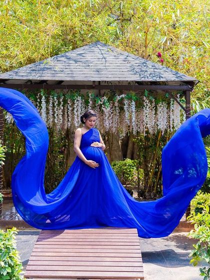 A solo maternity portrait with a flowing blue gown at the garden gazebo.