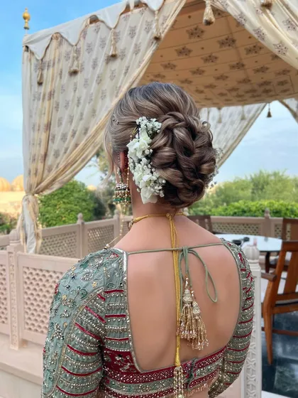 A textured low bun with interwoven braids, decorated with white flowers. This updo is perfect for a bride looking for a detailed and romantic hairstyle.