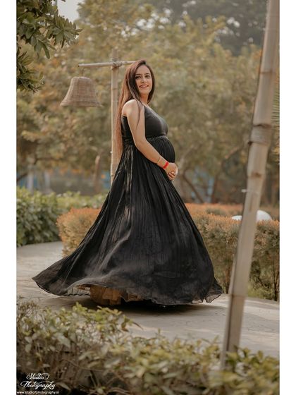 A joyful, twirling motion captured in a still photo. The movement of the black gown adds a dynamic and carefree feel to this outdoor maternity portrait.