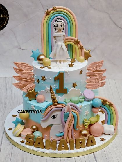This two-tier choco-chip unicorn cake is a dream come true for a first birthday. It features a large fondant unicorn head, rainbows, angel wings, and a custom nameplate for a personalized fantasy cake.