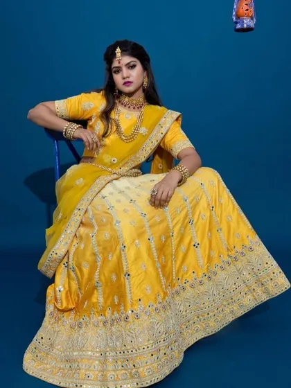 A model showcasing a traditional yellow and off-white lehenga with intricate mirror work. This outfit is an excellent choice for haldi ceremonies or festive wedding events, complete with matching jewelry.