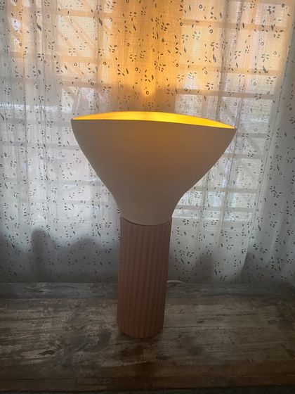 This table lamp is a combination of two separate ceramic forms. The base is a fluted terracotta cylinder, and the top is a smooth, wide stoneware shade, creating a warm, ambient glow.