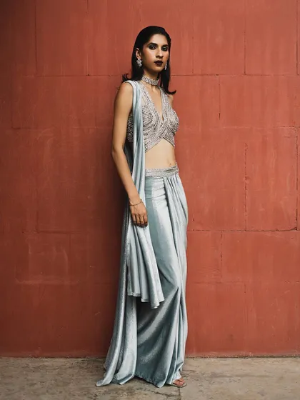 A festive lookbook shot against a bold red wall. The silver-grey sari creates a stunning color contrast, making the outfit stand out.