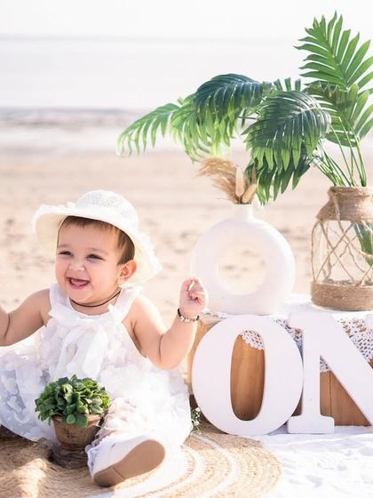 A happy baby girl enjoying her beach birthday party. The little sun hat and lace details on her dress add to the boho charm.