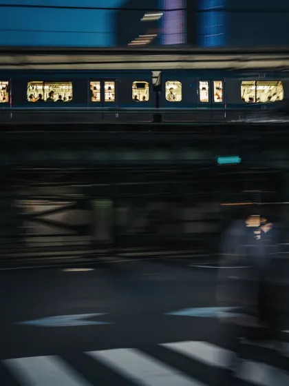 A motion blur shot capturing the energy of Tokyo at night, with a passing train above and a pedestrian in motion below. This technique transforms a simple street scene into a dynamic, abstract piece of art.