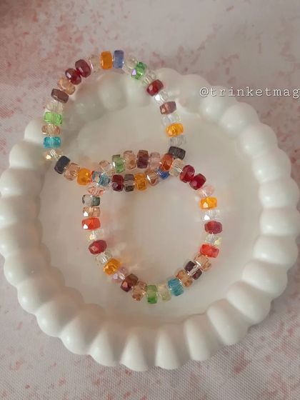 A pair of colorful, multi-faceted crystal bead bracelets resting in a decorative dish. These bracelets catch the light beautifully and add a rainbow of sparkle to your wrist.