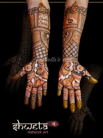 An intricate mehendi design for an engagement. The pattern includes the couple's initials and a wedding ring motif, surrounded by detailed floral and geometric work.