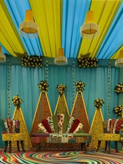 A closer view of the quirky Mehendi stage. The furniture is upholstered with patchwork fabric, and the backdrop is made of woven marigold flowers, combining modern and traditional elements.