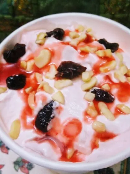 A delicious bowl of creamy vegan dessert, possibly a fruit-flavoured yogurt or nice-cream. It's topped with crunchy nuts, sweet raisins, and a drizzle of fruit syrup for a delightful treat.