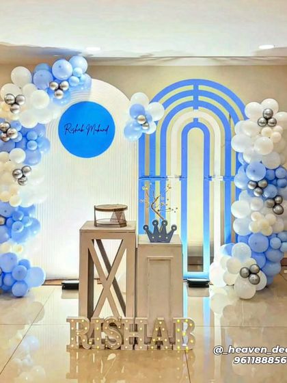 A modern and clean birthday setup using geometric arched backdrops in blue and white. The decor is completed with a simple balloon garland and rustic wooden plinths.