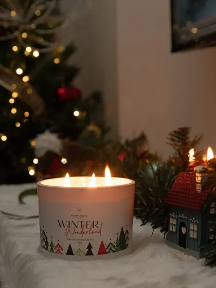 Our 'Winter Wonderland' three-wick candle glows in front of a Christmas tree. This festive candle is designed to fill your home with the scents of the season, making it a perfect holiday accessory.