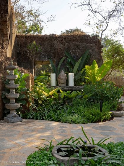 A serene nook within the ruins of Sanctuary Bar, featuring a Buddha head, candles, and a traditional stone lamp. The planting is dense and tropical, creating a spiritual and meditative corner.