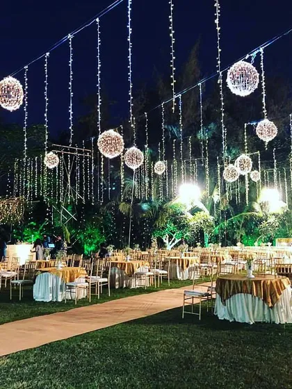 This image captures the magical ambiance of an outdoor reception at night. The lawn is illuminated by strings of fairy lights and hanging light globes, creating a dreamy and romantic setting for guest seating.