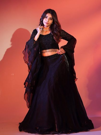 A full-length shot of the black lehenga, showing off its flowing skirt and dramatic silhouette against a warm, glowing background.